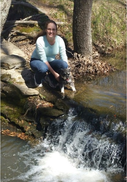 woman and a dog on a hike squatting by a small waterfall