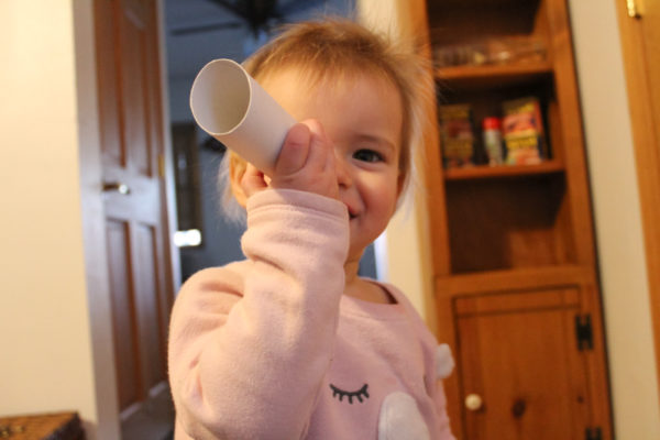girl holding toilet paper tube play an auditory-visual observation activities game