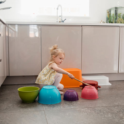 girl modeling auditory observation activity by banging on bowls with a wooden spoon